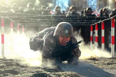 A Chinese soldier low-crawls in the dirt under barbed wire during training.