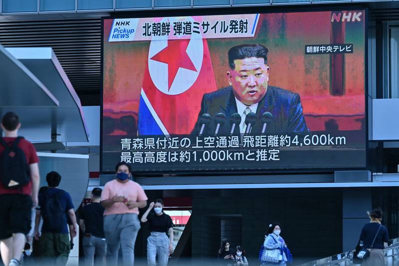 Pedestrians walk under a large video screen showing images of North Korea's leader Kim Jong Un during a news update in Tokyo on Oct. 4, 2022.