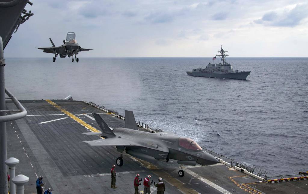 An F-35B Lightning II approaches the amphibious assault ship USS Wasp as the guided-missile destroyer USS Dewey is seen alongside it.