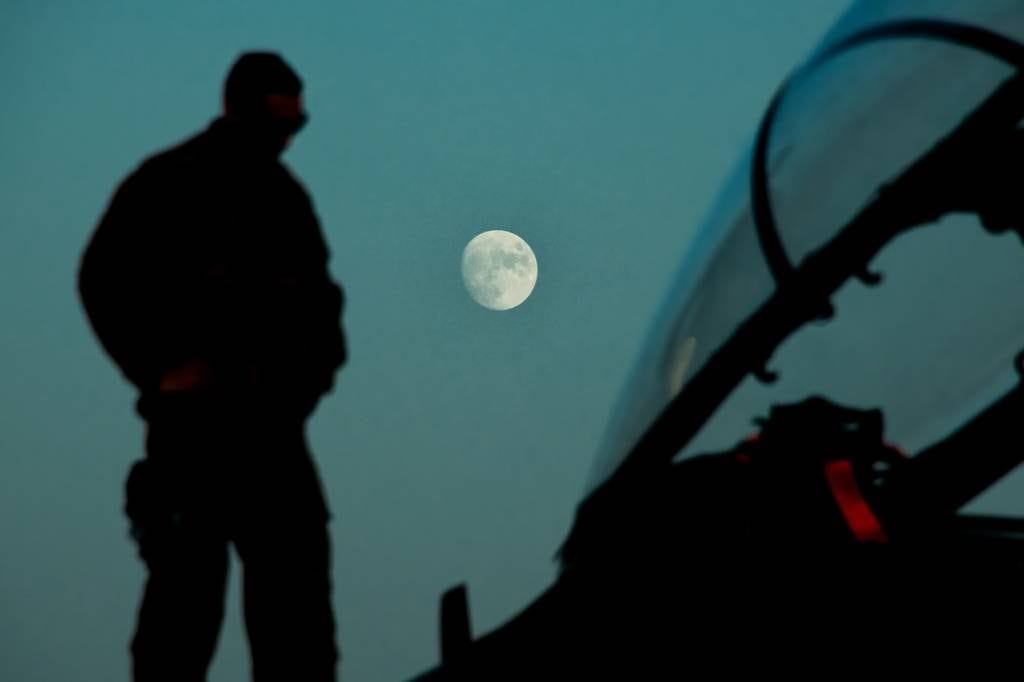 A maintainer deployed to the 332d Air Expeditionary Wing, checks an F-15E Strike Eagle during a routine post flight inspection Sept. 29, 2020, as the moon rises over the flightline in an undisclosed location.
