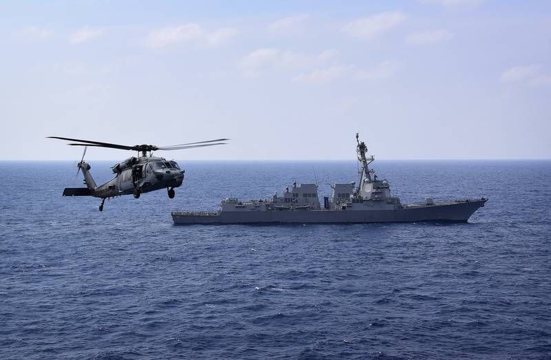 An MH-60S Sea Hawk helicopter flies past the guided-missile destroyer USS Sterett.